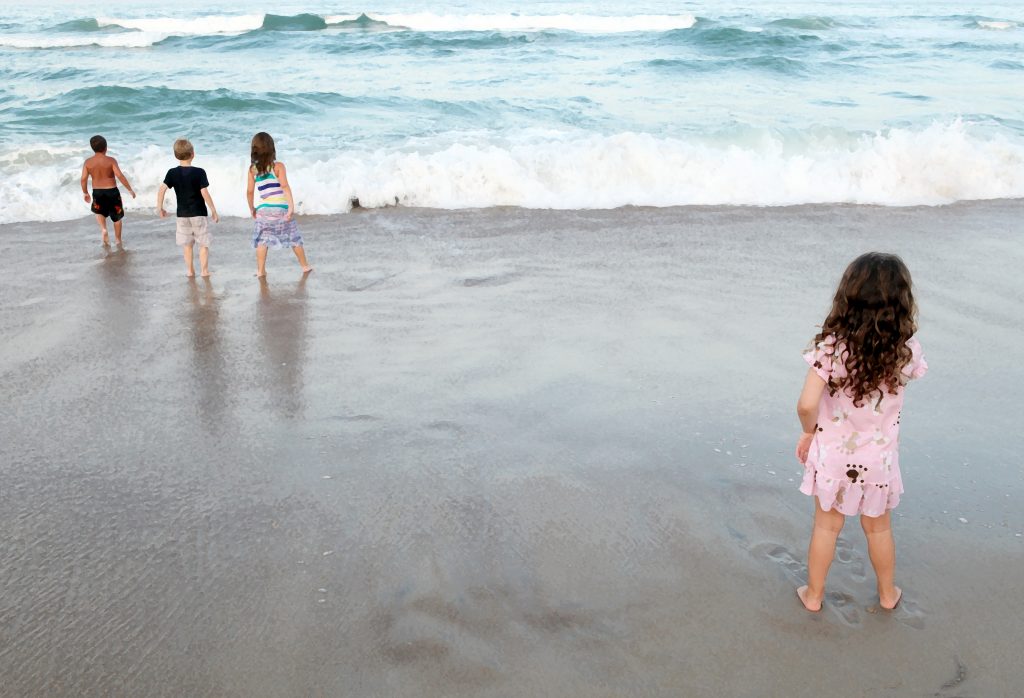 one child stands apart from three children playing in the ocean