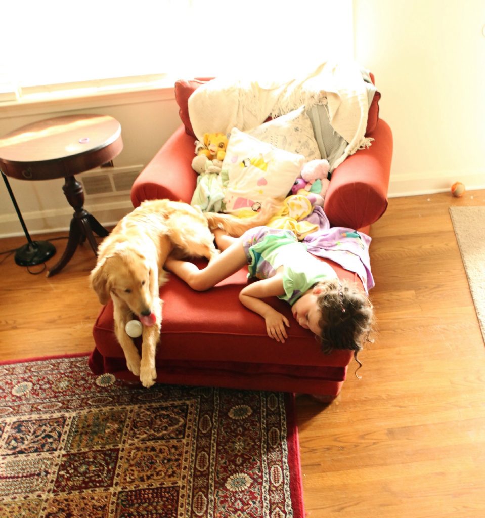 child in pajamas lying on red chair with dog